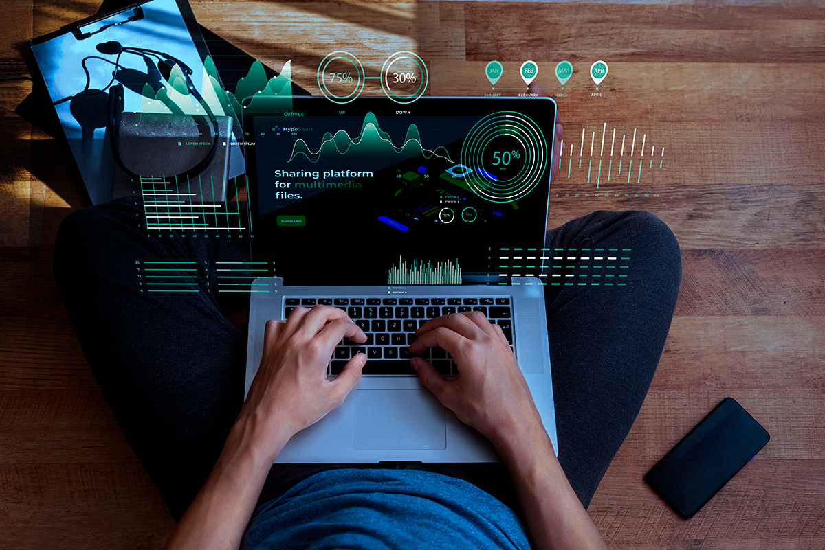 A person working on a laptop with digital data visualizations, charts, and analytics overlaid on the screen, representing real-time monitoring.